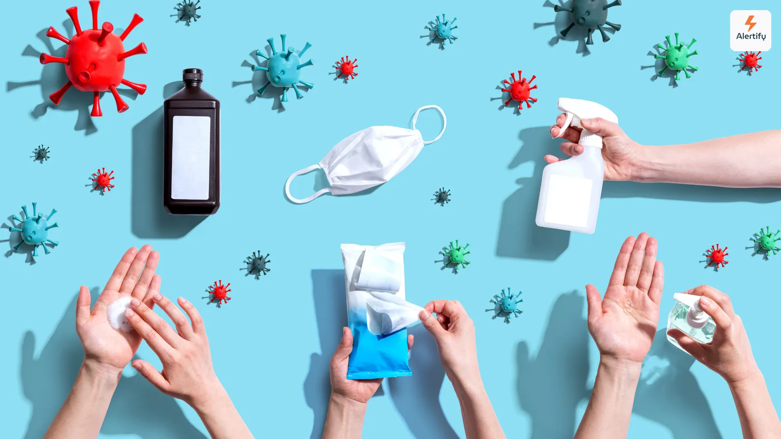 Vista dall'alto di modelli di virus, una mascherina, uno spray igienizzante e mani che usano prodotti per l'igiene