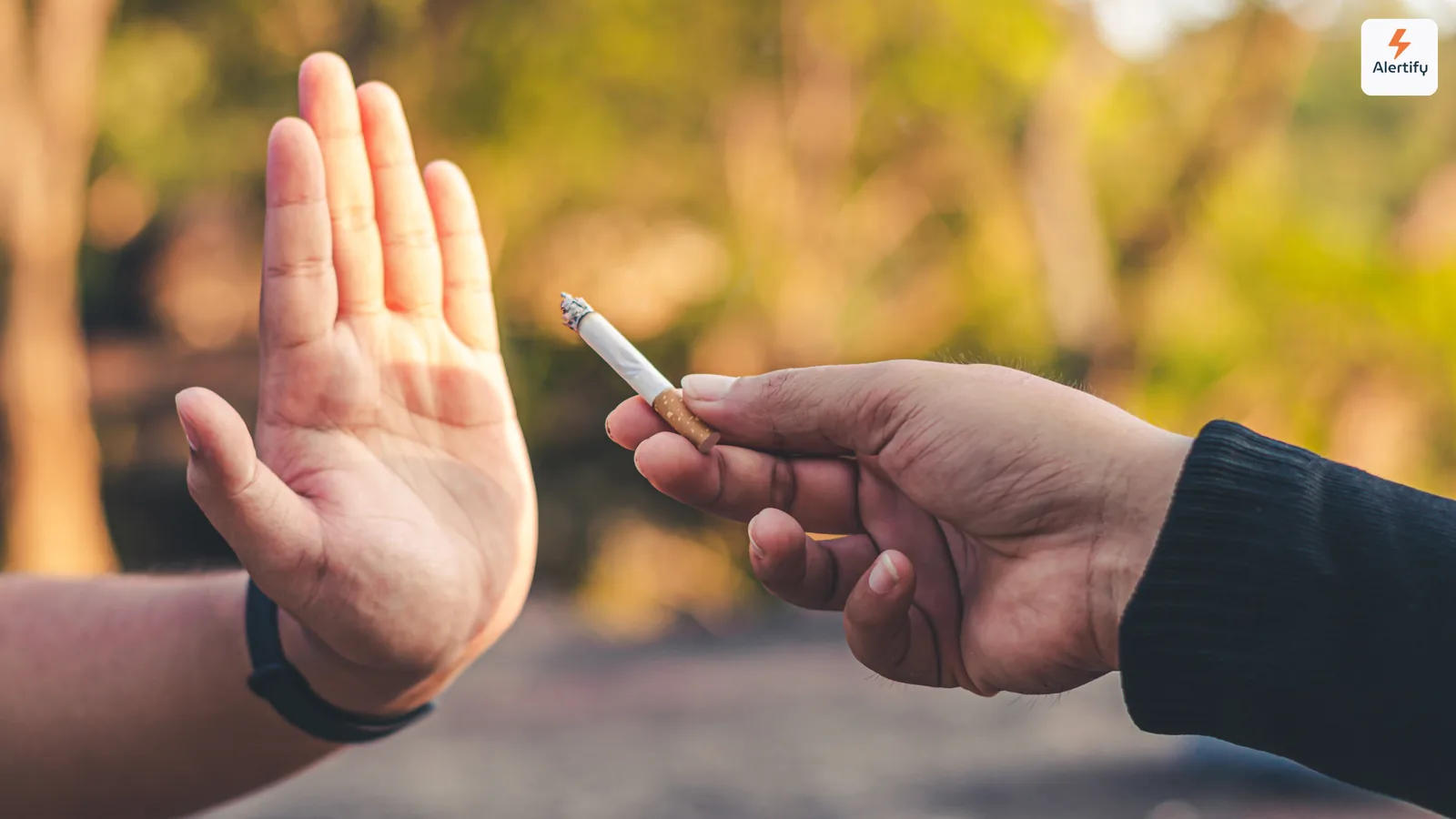 Mano alzata per rifiutare gentilmente una sigaretta accesa offerta da un'altra persona all'aperto