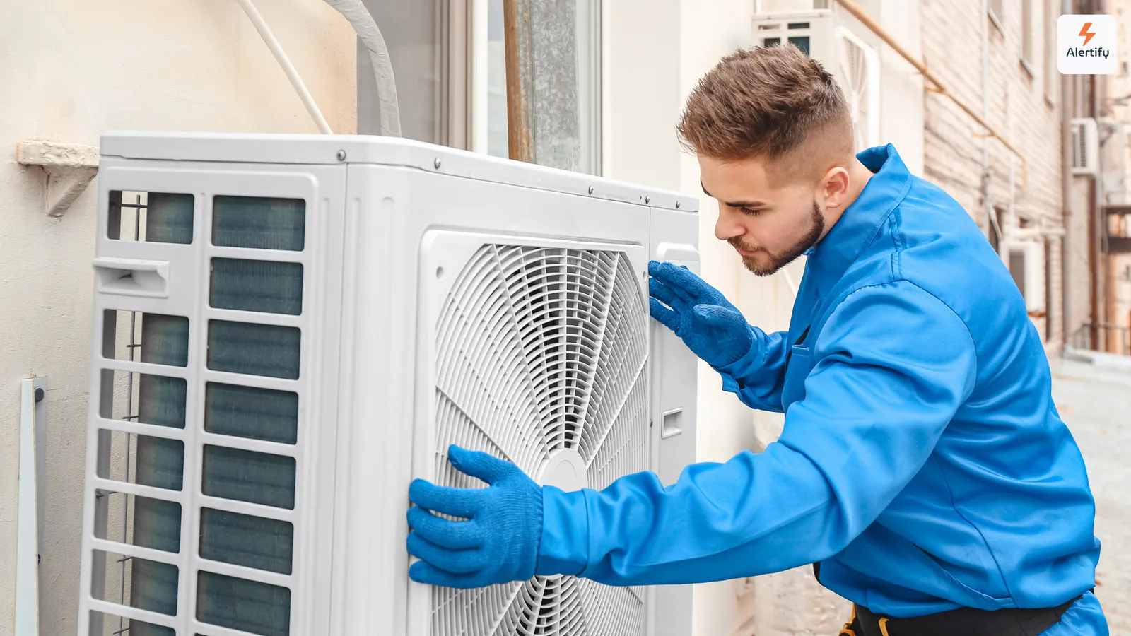 Tecnico HVAC in tuta blu e guanti al lavoro su un'unità esterna di climatizzazione